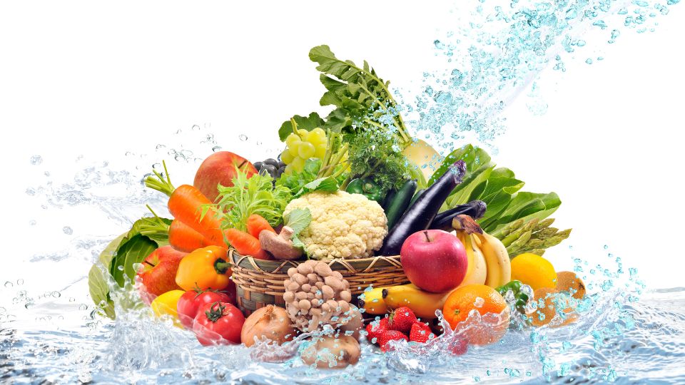 Ein Korb voller frischer Gemüse und Obstsorten, umgeben von spritzendem Wasser.