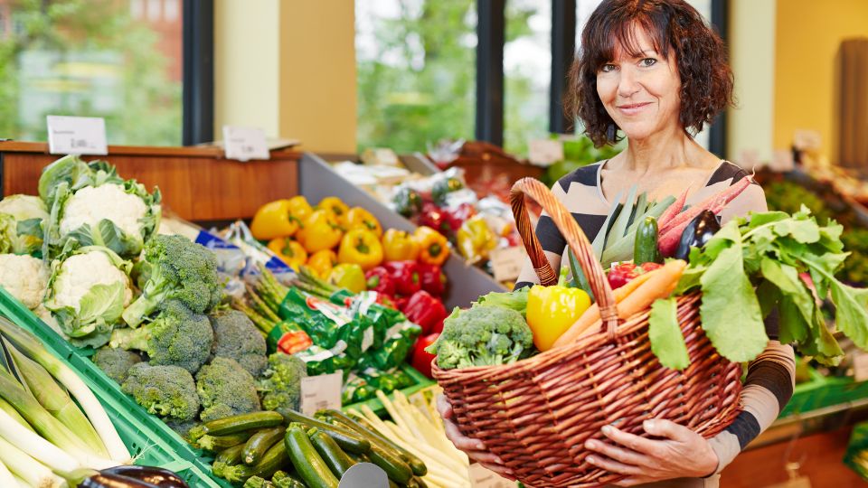 Eine Frau hält einen Korb voller frischem Gemüse in einem Markt.