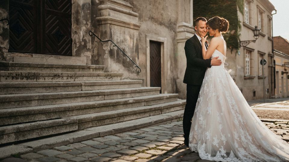 Ein Brautpaar steht vor einer Kirche und lächelt sich an, umgeben von einer romantischen Atmosphäre.