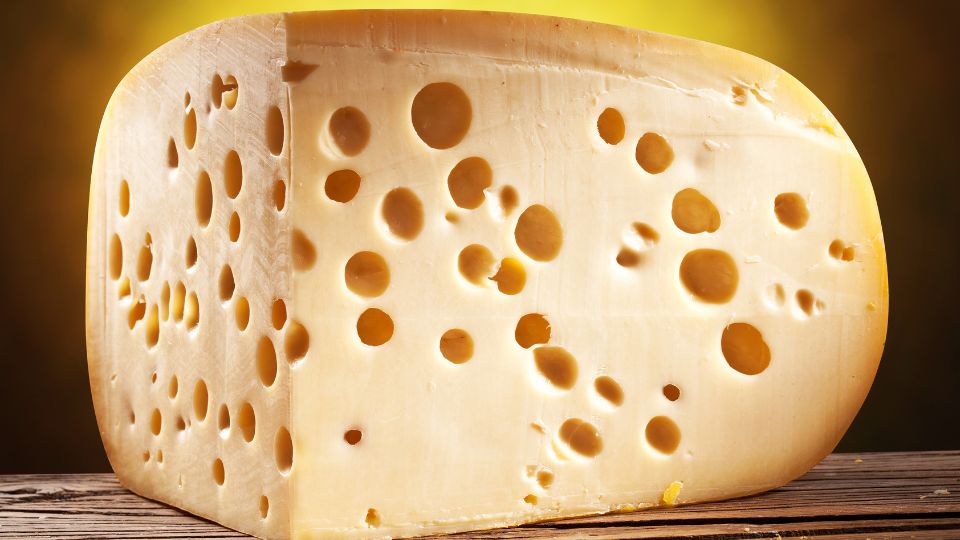 Ein Stück Ementaler Käse mit charakteristischen Löchern auf einem Holztisch.
