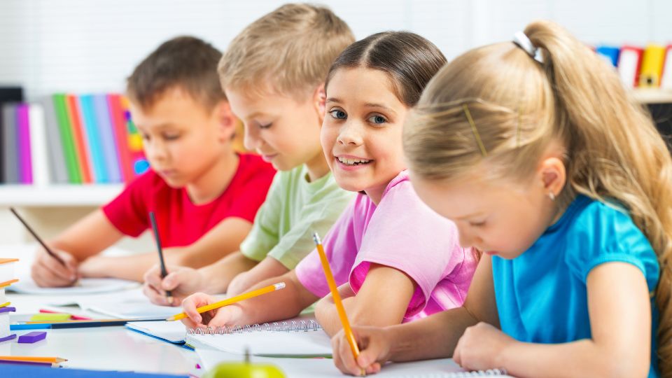 Vier Kinder zeichnen konzentriert an einem Tisch mit Stiften und Papier.