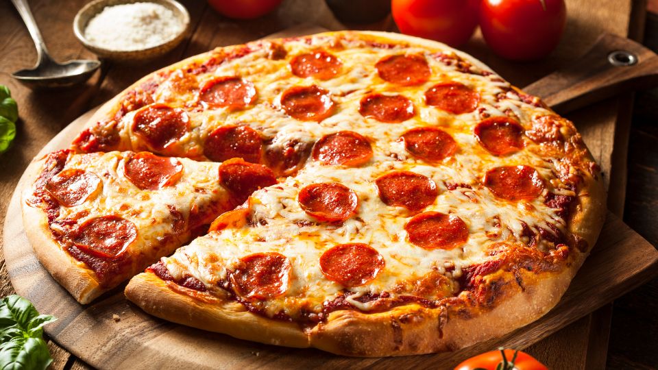 Eine frisch gebackene Pizza mit Salami und Käse auf einem Holzbrett.