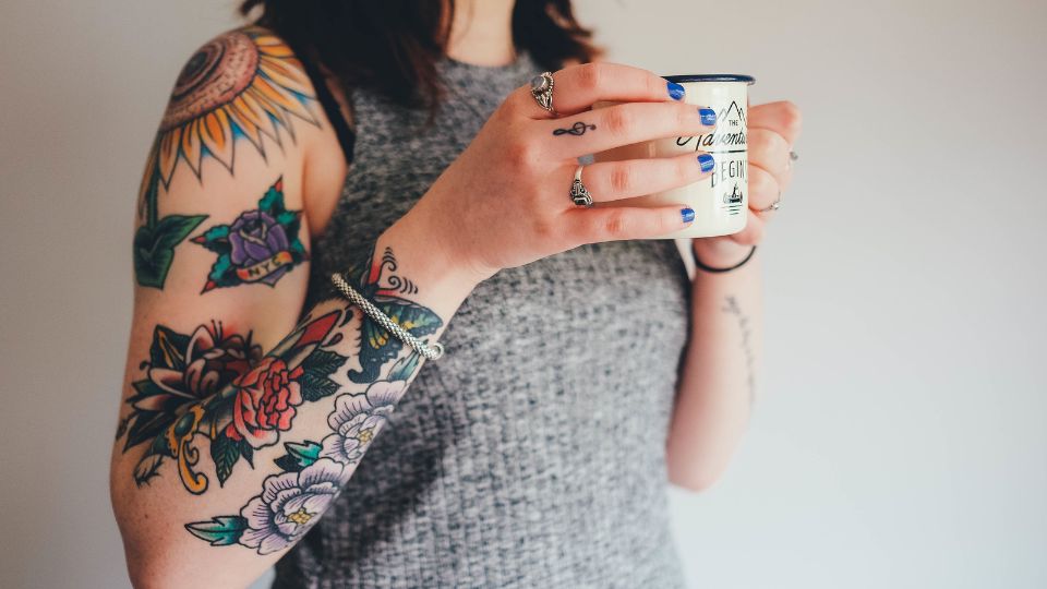 Eine Frau mit bunten Tattoos auf dem Arm hält eine Tasse in der Hand.