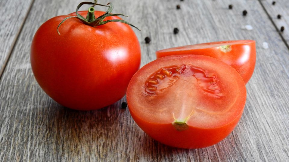 Eine frische, rote Tomate und eine halbierte Tomate auf einem Holztisch.