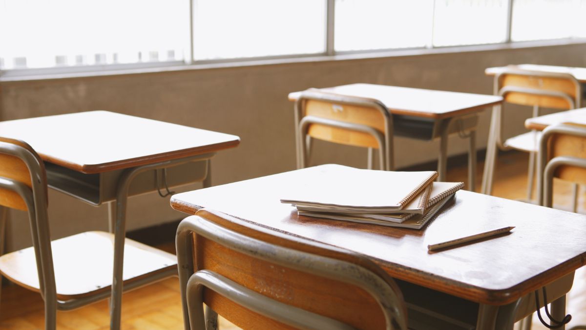 Ein leerer Klassenraum mit Schulbänken und Notizblöcken auf einem Tisch.